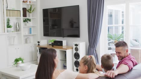 happy caucasian parents, son and daughter on couch watching tv, copy space on screen