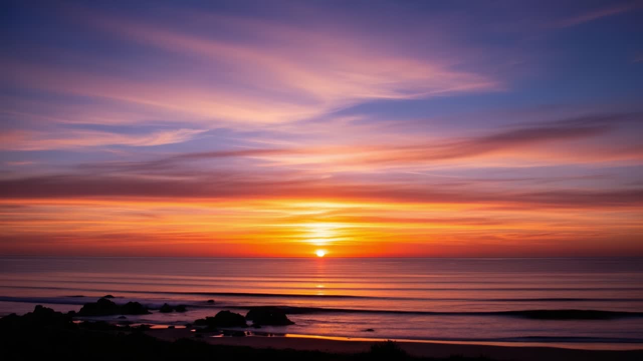 En betagende solnedgang over rolige vande: En afslappende udsigt til naturens aftenpalet med levende farver og fredfyldte bølger, der spejler den uendelige himmel.