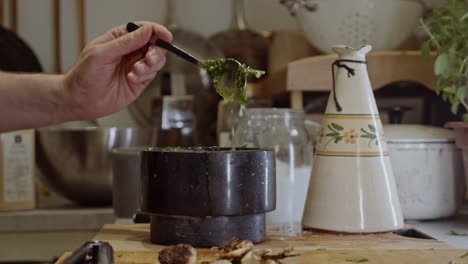 revolviendo con una cuchara de metal una salsa saludable con hierbas en un tazón negro de cerámica