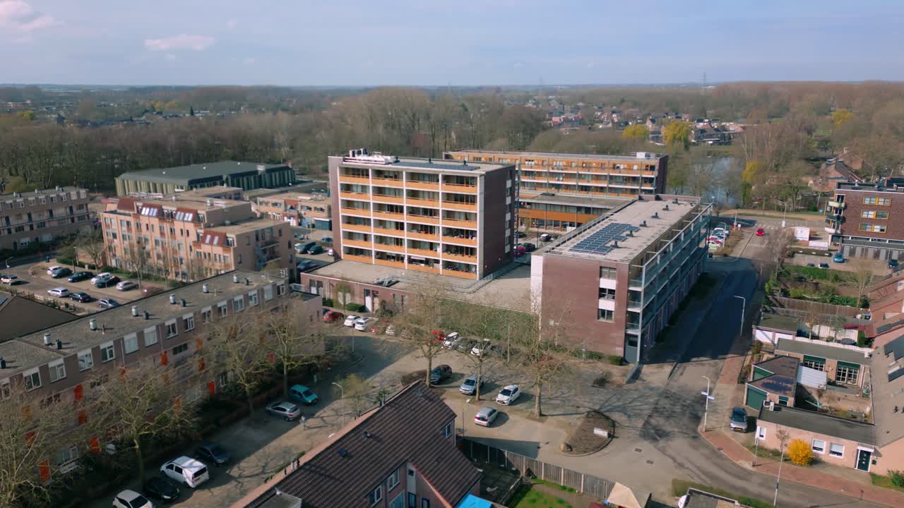 Amplia vista aérea de un vibrante barrio residencial. Edificios de apartamentos modernos se alzan entre numerosas casas y exuberantes árboles verdes. Numerosos coches aparcados a lo largo de las calles, creando un ambiente bullicioso