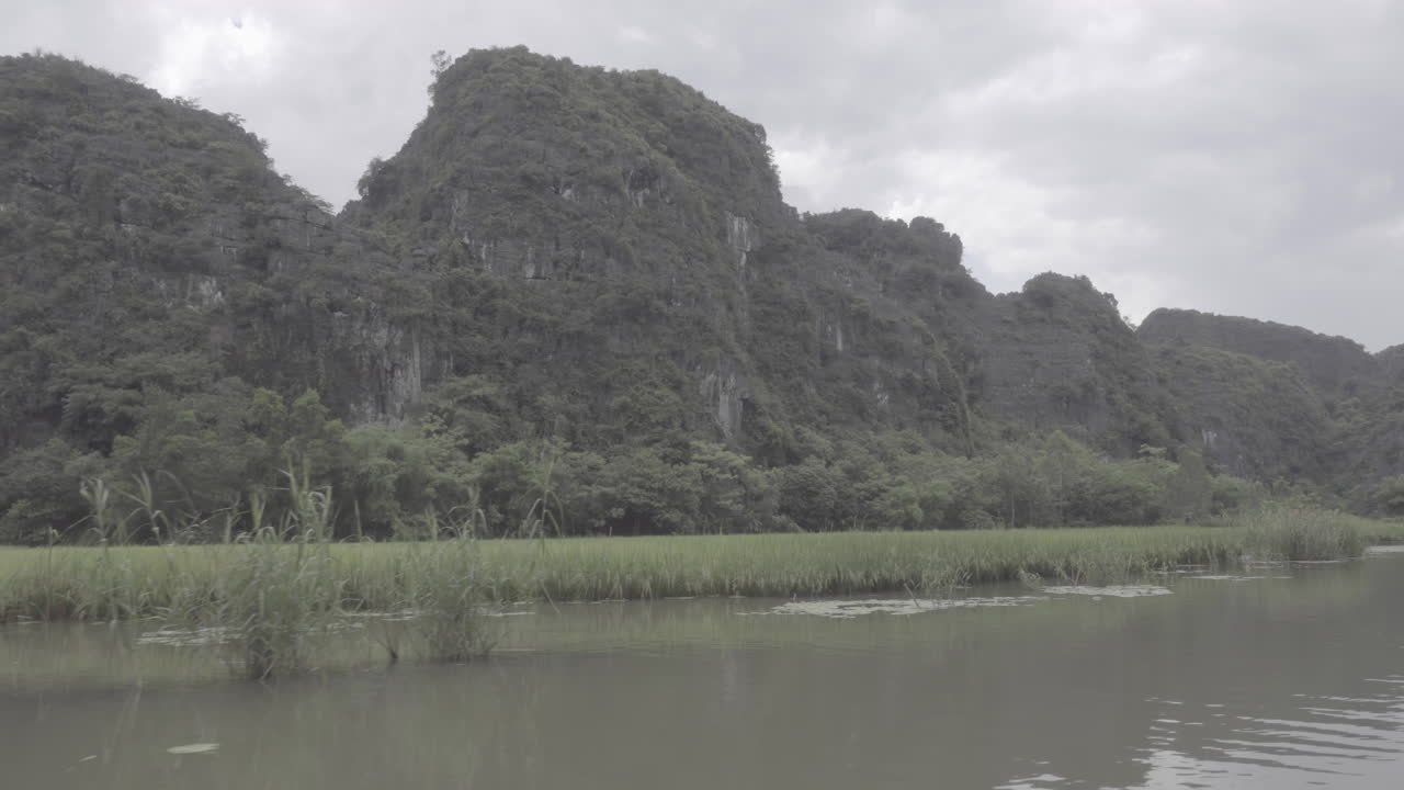 navegando a través de los campos de arroz en vietnam en un barco turístico durante un día nublado con montañas y rocas