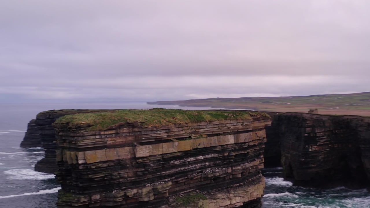 Aerial orbit of Dun Briste sea stack with Downpatrick Head coastline behind revealing waves crashing on rocks