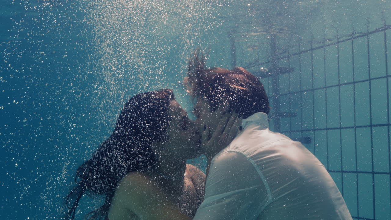 로맨틱한 커플이 수영장에서 물속에서 키스하고 옷을 입고 사랑하는 젊은이들이 친밀한 키스를 즐기고 사랑하는 사람들이 물에 잠겨 거품으로 떠다니며 열정적인 친밀감을 느끼고 있습니다.