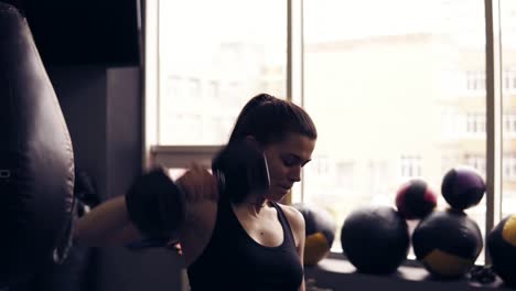 Attractive-young-brunette-female-workouter-lifting-up-dumbbells-at-the-gym.-Achieving-perfect-body-shape.-Endurance,-concentration.