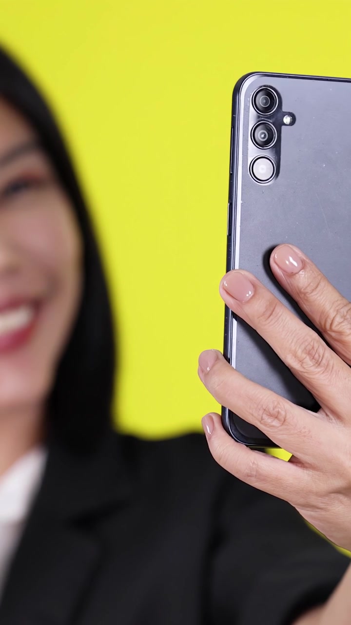 Donna sorridente in blazer nero reagisce con sorpresa durante una videochiamata, sfondo giallo vibrante