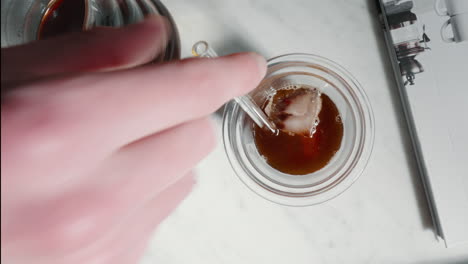 hand stirring iced coffee in transparent glass on marble surface