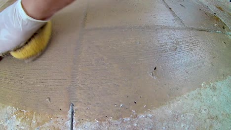 Grouting stone tile, gloved hand rubs grout in cracks then wipes with sponge
