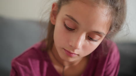 close up of cute girl in maroon top lost in thought with gentle expression as she gazes downward in quiet moment of focus and reflection on soft indoor background