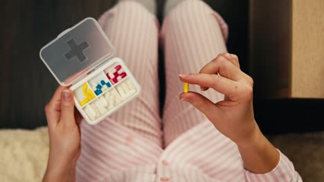 woman in pajamas holding pill organizer and taking a pill