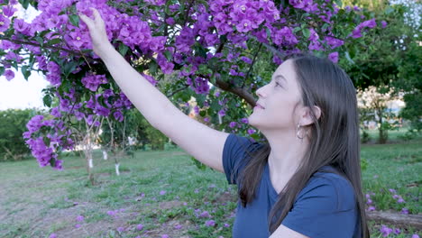 Caucasian-woman-sitting-happy-in-park-picks-flower-from-tree-and-smells-it