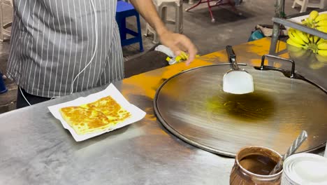 un vendedor callejero en phuket prepara y sirve roti de plátano, mostrando técnicas tradicionales de comida callejera tailandesa en un entorno vibrante