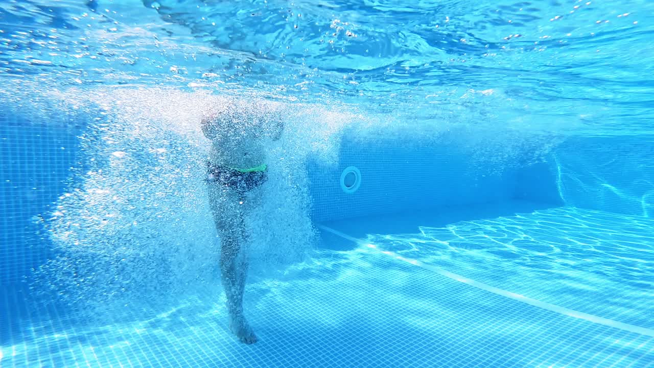 Boy jumping into the clear water in the swimming pool. Young guy jumps underwater on a blue background. Water with bubbles inside the pool.