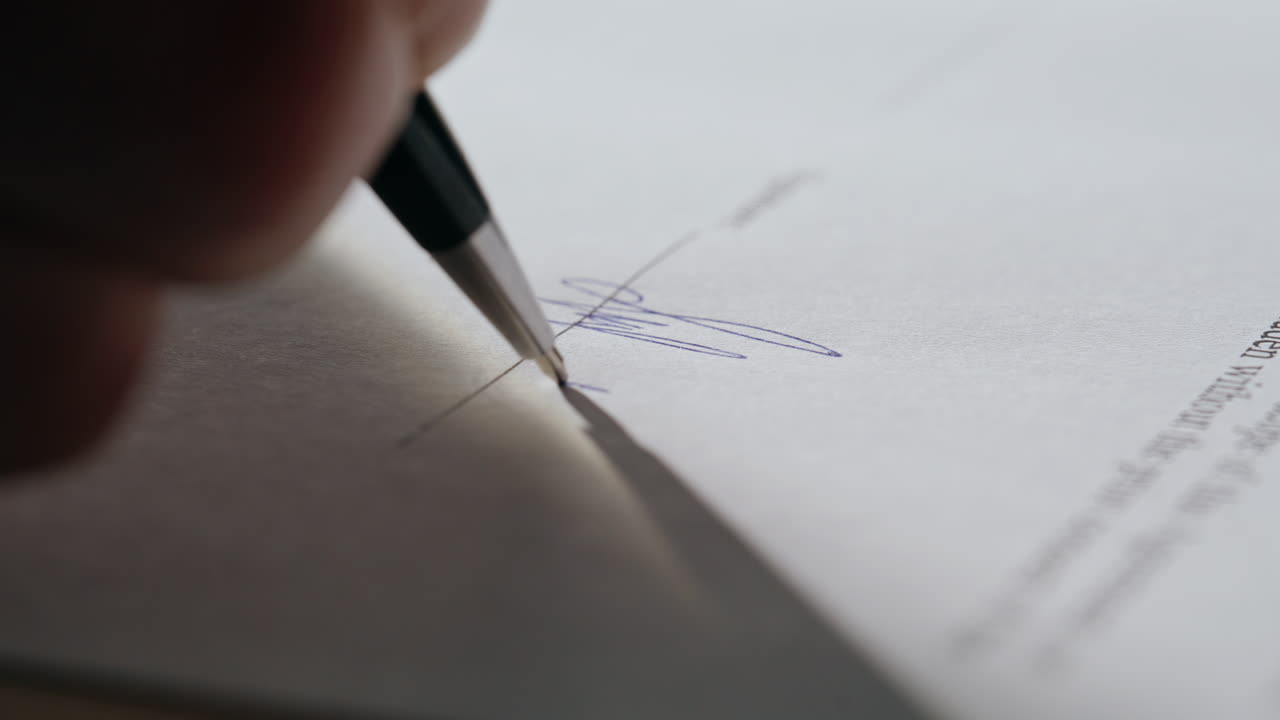 Primo piano di una mano che firma un documento su una scrivania d'ufficio. Un uomo d'affari appone la sua firma