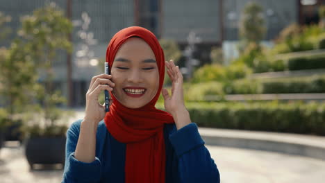 young muslim woman in hijab talking on phone outdoors