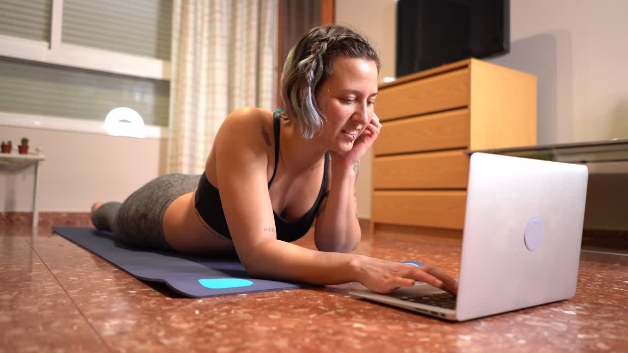 Woman smiles stretched out on the mat operating the computer ready to play sports