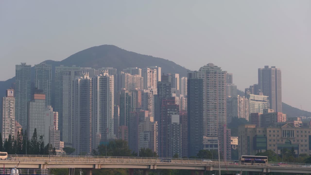 Vista panoramica delle strutture portuali lungo il Victoria Harbour nel centro di Hong Kong in una giornata di sole, con navi, terminal e lo skyline urbano