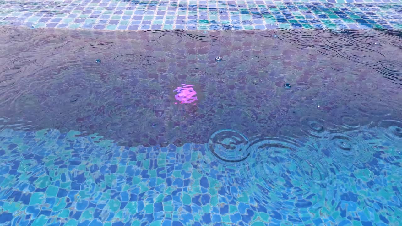 Gotas de chuva caindo na superfície da água de uma piscina de azulejos azuis em um dia chuvoso na Tailândia.