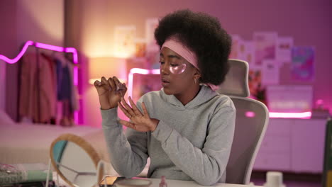 young african american woman applying nail polish while sitting in a chair in her bedroom