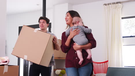 family with baby carrying removal boxes into new home on moving day