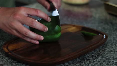 cutting and removing the seeds on a green bell pepper on a wooden cutting board