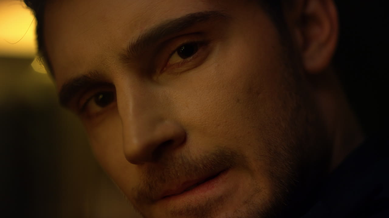 hermoso rostro de hombre mirando a la cámara en el interior. hombre elegante mordiendo el labio habitación oscura