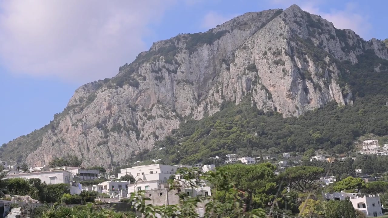 Antenne per telecomunicazioni e case bianche mediterranee si trovano sotto una collina rocciosa di Capri con pini che si muovono in una leggera brezza