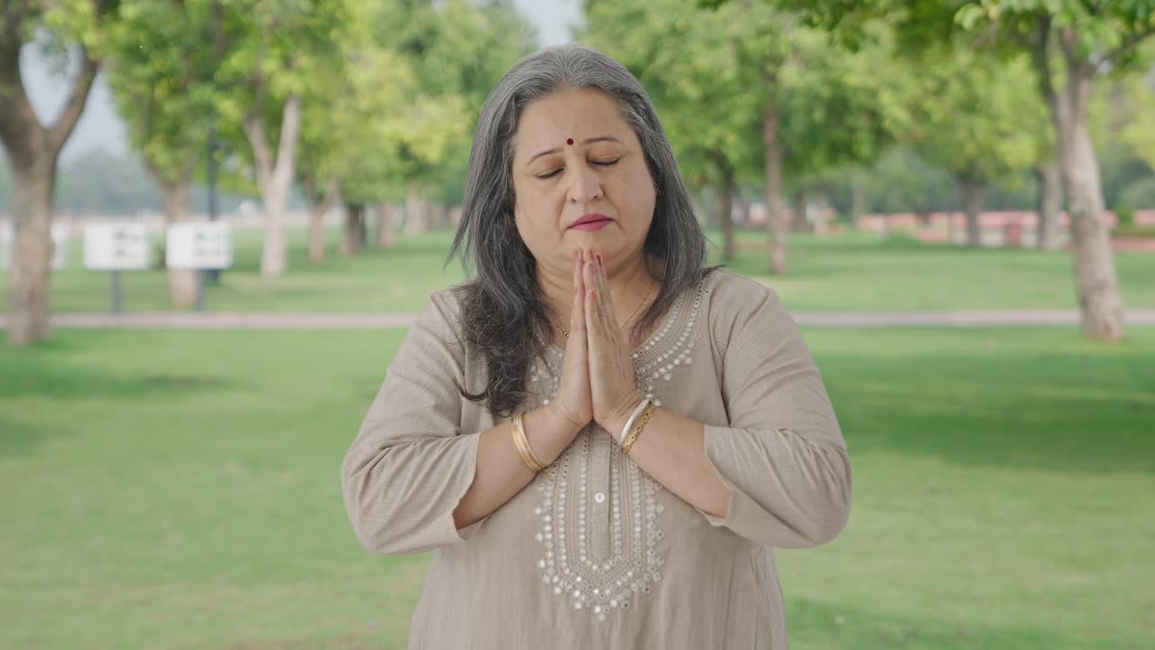 Religious Indian old woman praying to God in park