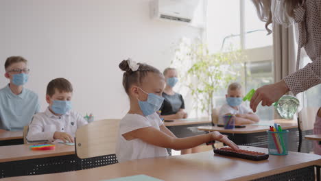 The teacher treats the hands of an antiseptic girl in the classroom at school before class. coronavirus and the pandemic at school. The work of the school in the epidemic mode