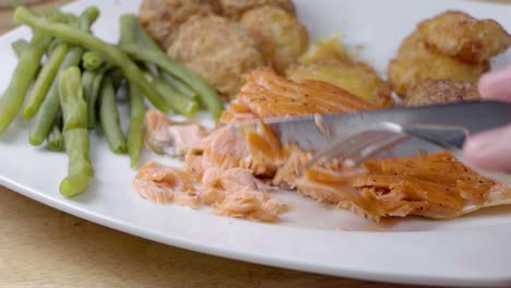 slow motion slider shot of eating a pan fried salmon fillet on a white plate with vegetables