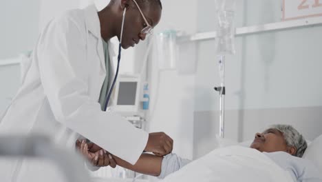 Diverse-female-doctor-using-stethoscope-on-arm-of-senior-female-patient-in-bed,-slow-motion