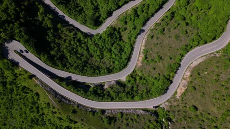 overhead drone shot of a winding mountain road with sharp hairpin curves cutting through green hills. shot at selvino, italy (selvino, italia)