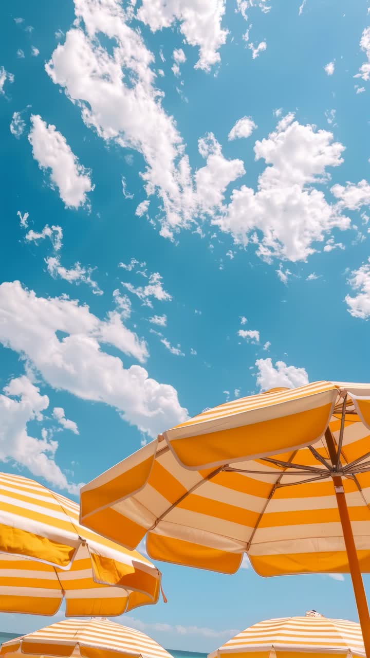 Vibrant video scene of yellow-striped umbrellas from a low angle against a bright blue sky