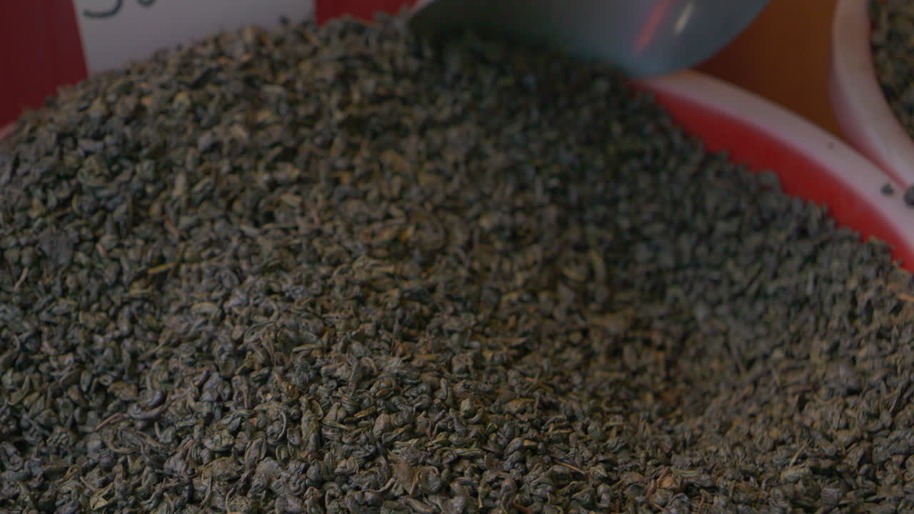 Close up video of loose leaf tea being scooped with a metal spoon from a large container dry curled leaves rich texture market food ingredient concept macro detail 4k