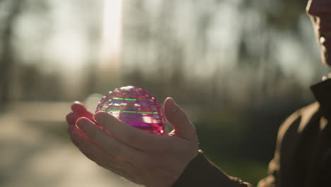 a close-up of an adult holding a small, colorful rotating object in his hands, carefully balancing it before letting it fall to the ground