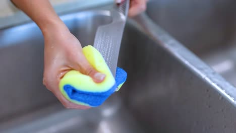a person cleans a knife with a sponge in a kitchen sink, highlighting effective cleaning techniques and safety