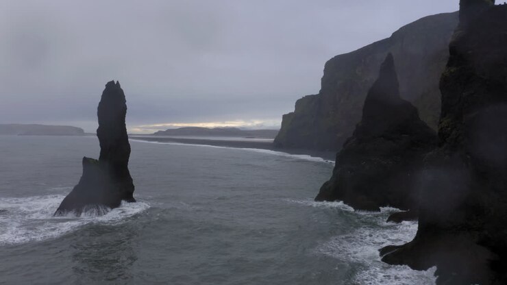 Aerial: Backwards reveal shot of Reynisdrangar sea stacks during bad weather