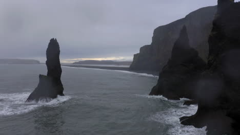 Aerial:-Backwards-reveal-shot-of-Reynisdrangar-sea-stacks-during-bad-weather