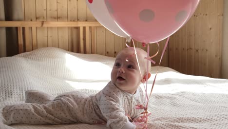 adorable baby girl lying on a bed. first birthday party. baby playing with pink balloons.