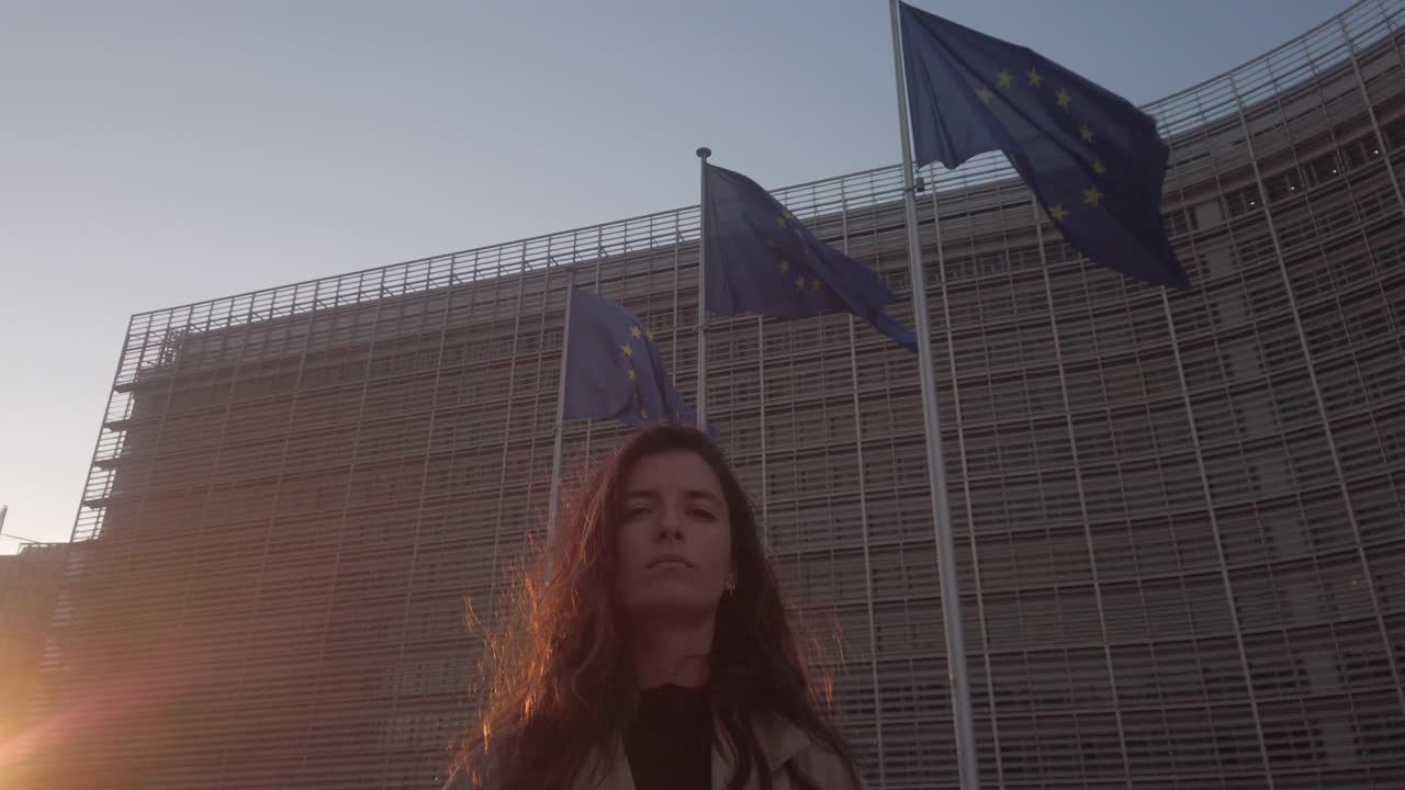Rallentatore di una donna di fronte al palazzo Berlaymont della Commissione europea con le bandiere dell'UE al tramonto