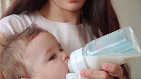 mother feeding baby boy from bottle at home