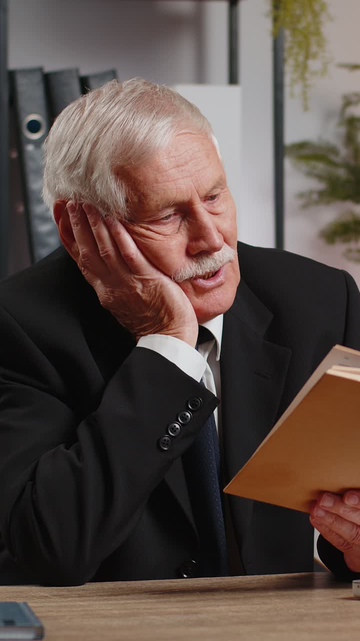 Bored caucasian senior businessman reading book literature taking a rest after work at table