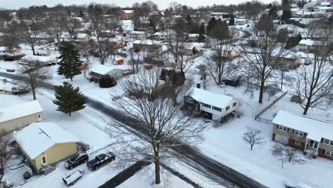 Aerial-view-of-snow-covered-neighborhood-with-roads,-trees,-and-houses-at-twilight