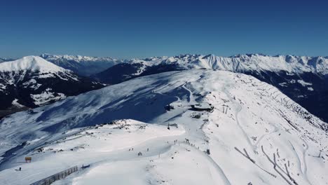 Ski-slope-with-skiers-on-mountain-ridge-in-the-Alps,-aerial