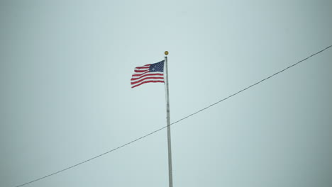 united states american flag blowing in the wind with snowflakes falling in slow motion winter snow storm