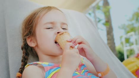 una niña feliz disfruta de las vacaciones de verano, se acuesta en un sofá en el mar y come un delicioso helado