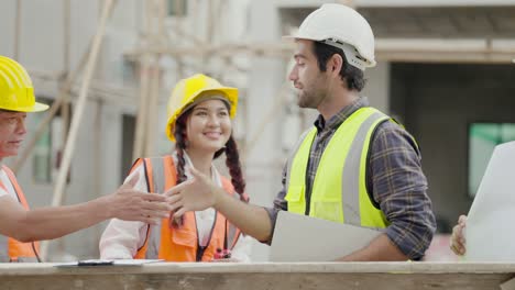 ingeniero reunión con el equipo contratista y capataz, hablar y explicar el modelo de construcción de viviendas en portátil y plano, estrechar la mano después de llegar a un acuerdo en el plan o en la forma de trabajo. trabajador que trabaja en el sitio de construcción en el negocio inmobiliario.