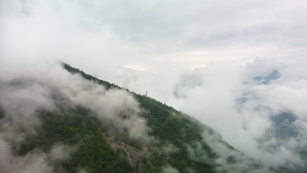 Drone footage moves in towards a tree covered mountain side that has low lying fog all around