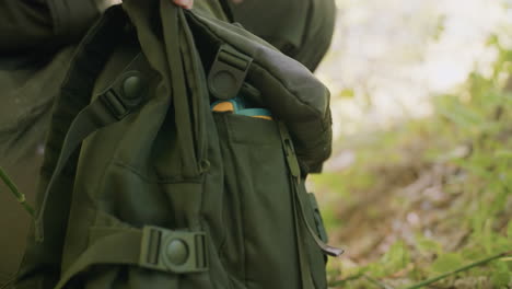 close view of tourist military boot marked with wear and side blurry view of grasses as tourist opens bag widely to retrieve rope and glove, preparing for the next move in an outdoor adventure