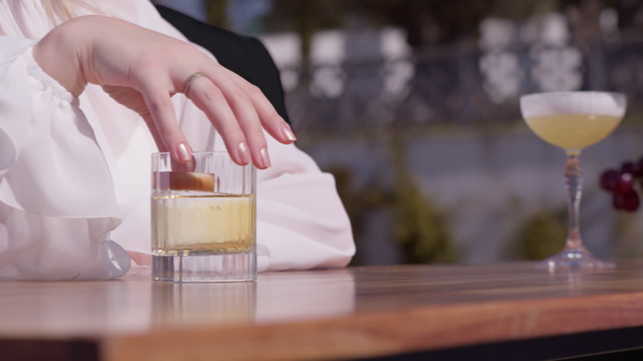 Woman's hand in white shirt pulling glass with drink from counter. Close up, pan left