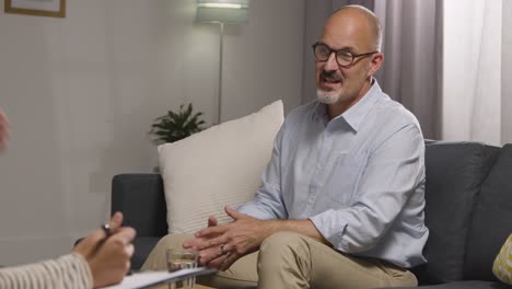 mature man sitting on sofa talking with counsellor about general or mental health issue